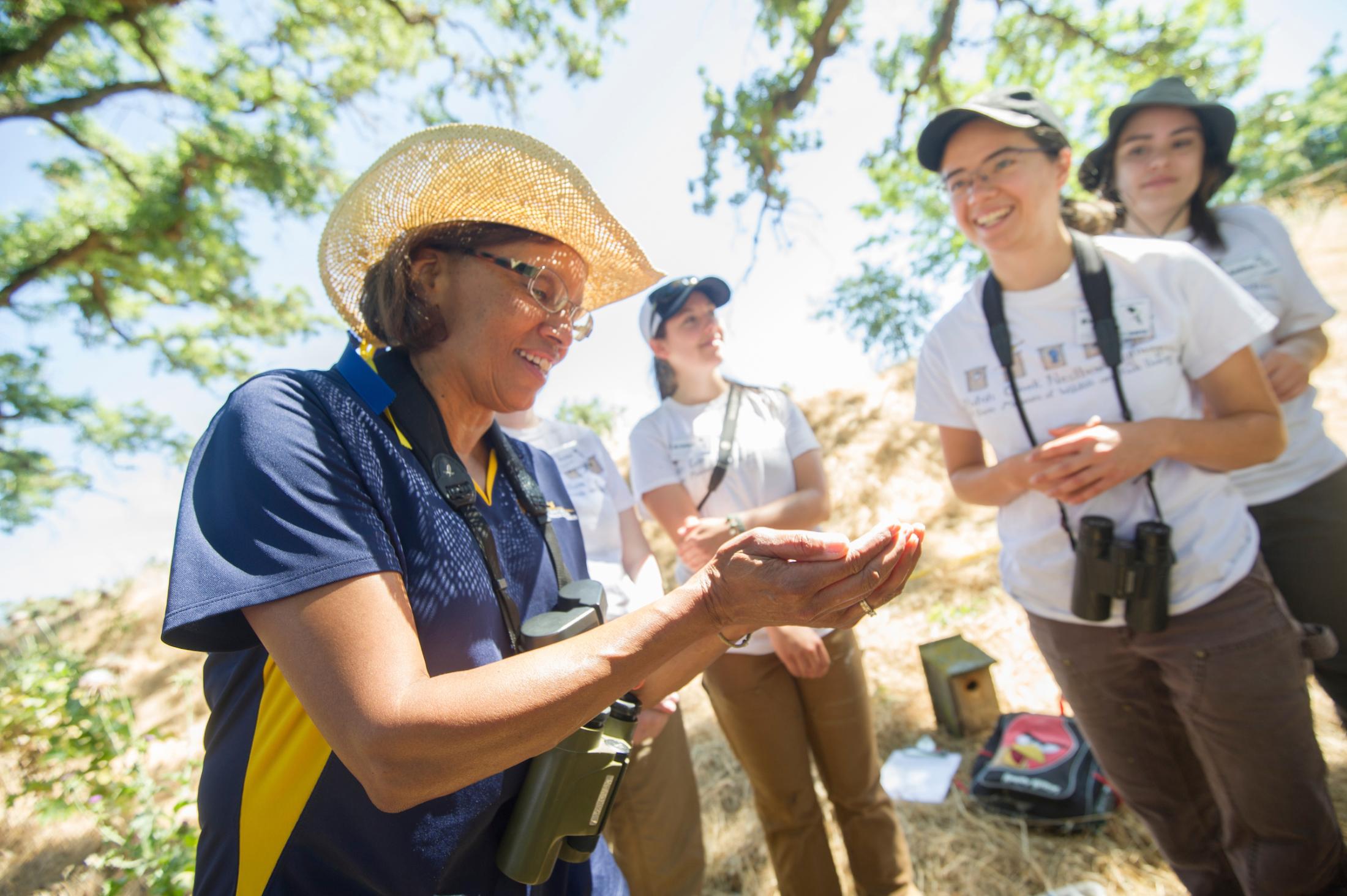 Woman wearing a hat in a field holds a bird with students looking